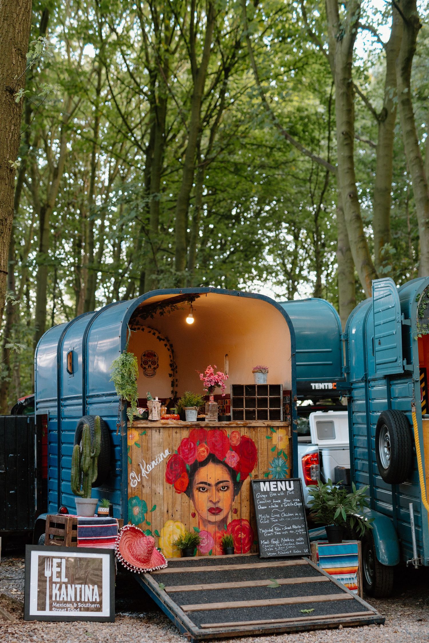 A colorful converted food trailer in a forest setting with Mexican-inspired artwork and menu board.
