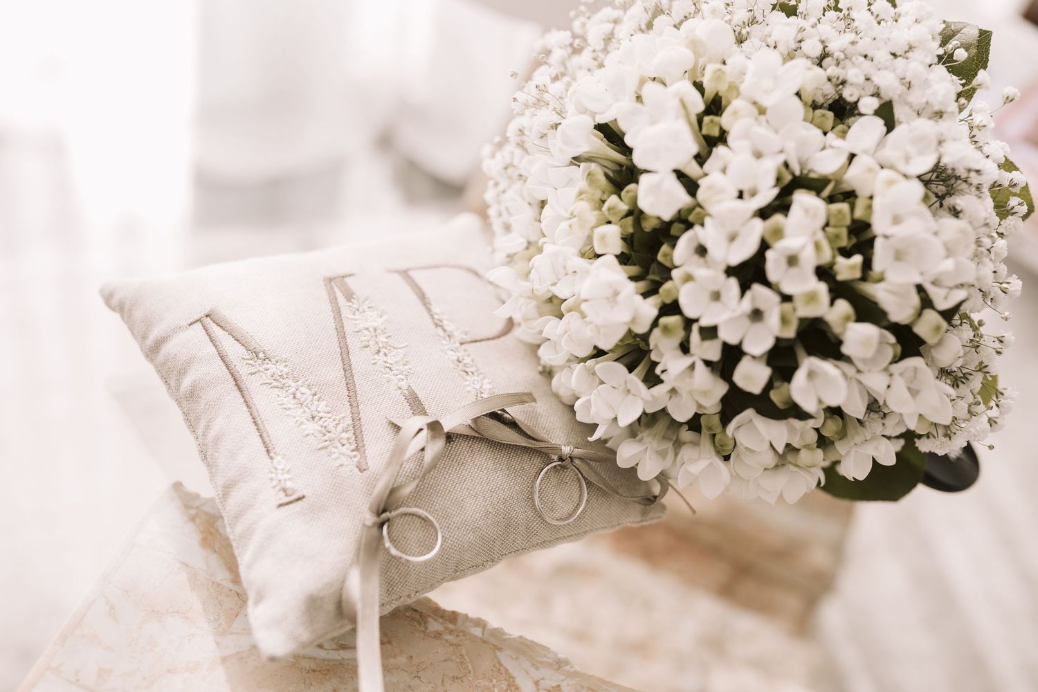 Cuscinetto ricamato con le iniziali e le fedi degli sposi accanto al bouquet verde con fiorellini bianchi