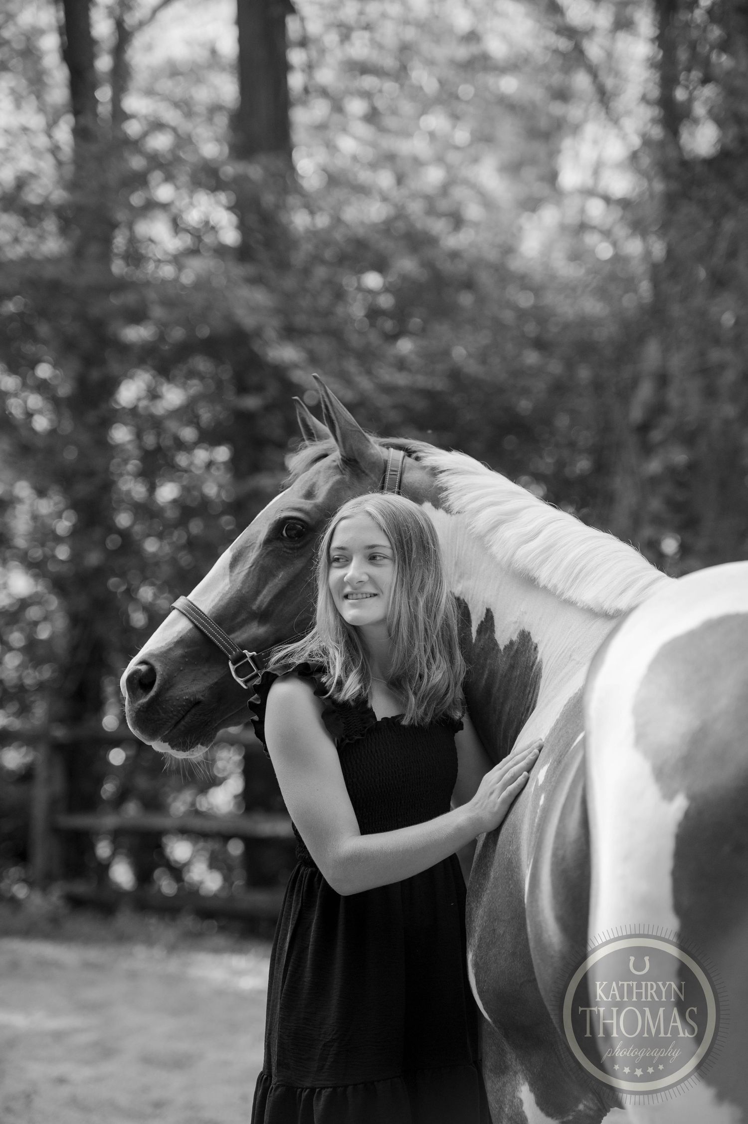 A monochrome portrait of a person with their horse outdoors in a natural setting.