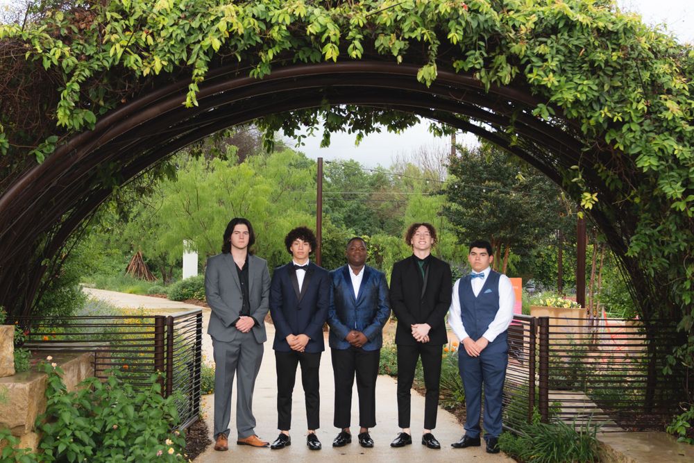 A group stands under a lush green garden archway in formal attire.