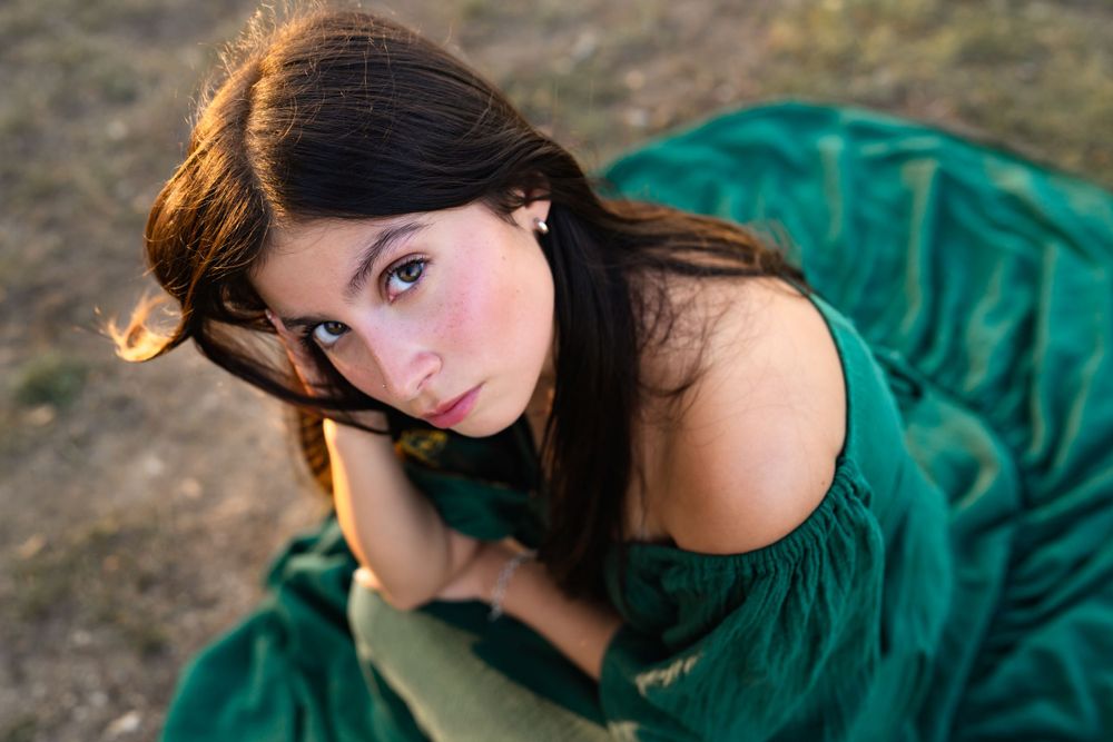 A person wearing an elegant emerald green dress poses outdoors during golden hour lighting.