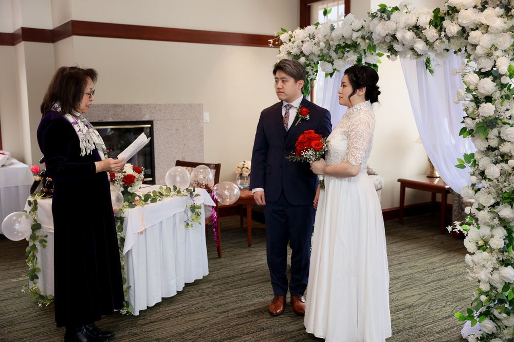 A couple exchanges vows during an indoor wedding ceremony under a floral arch with white flowers. smilein wedding photography