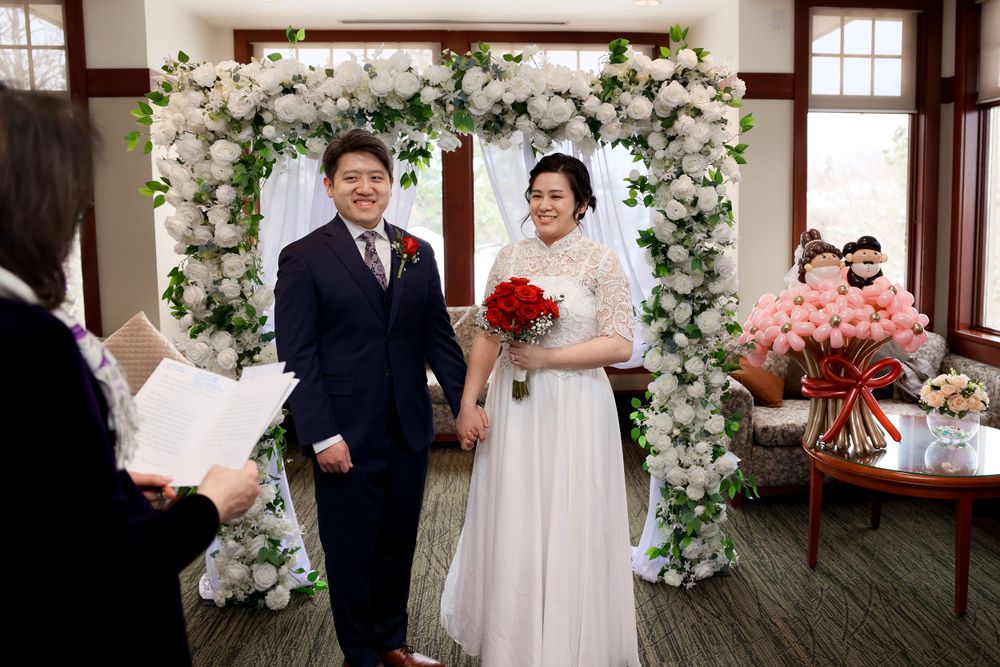 A wedding ceremony setup with a beautiful floral arch made of white flowers and greenery in an indoor venue. smilein wedding photography