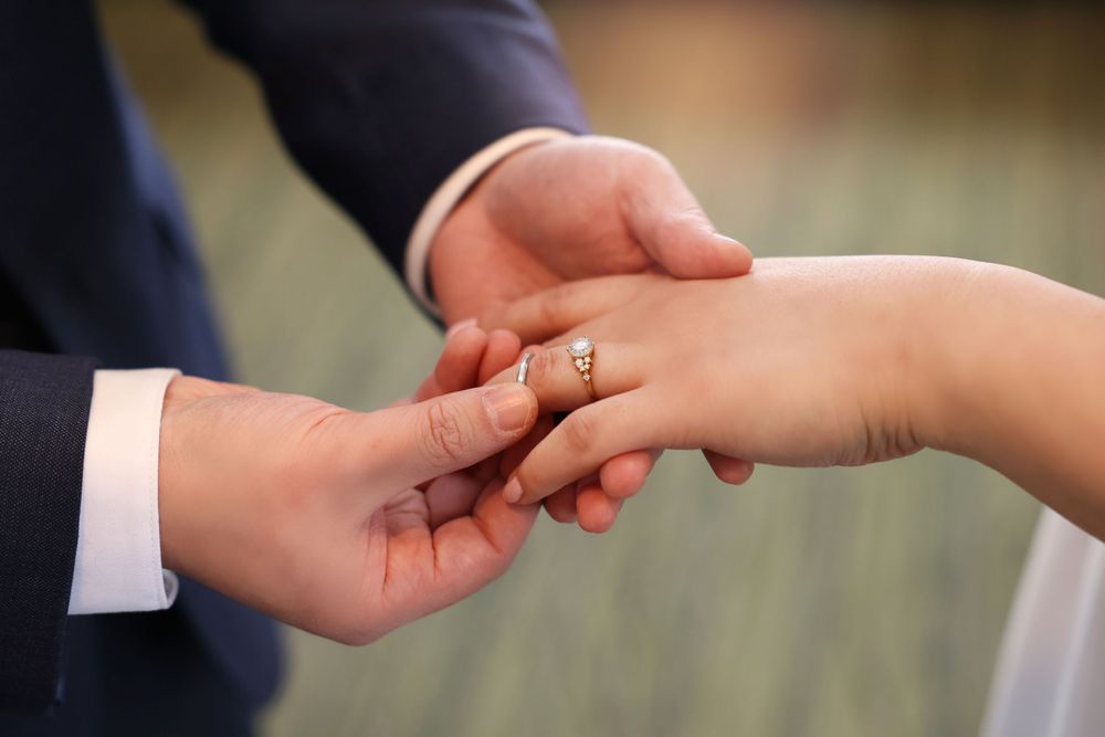 Close-up of hands exchanging wedding rings during marriage ceremony with diamond ring visible. smilein wedding photography