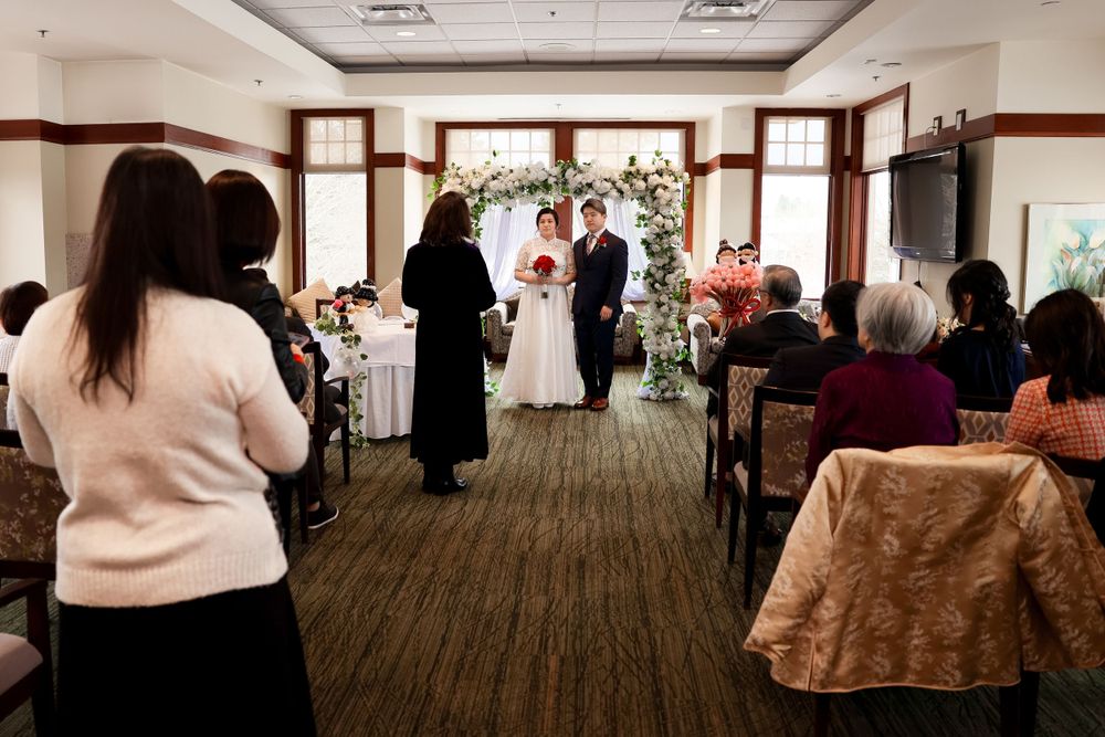 Wedding guests observe an indoor marriage ceremony from wooden chairs in an elegant venue with warm lighting. smilein wedding photography