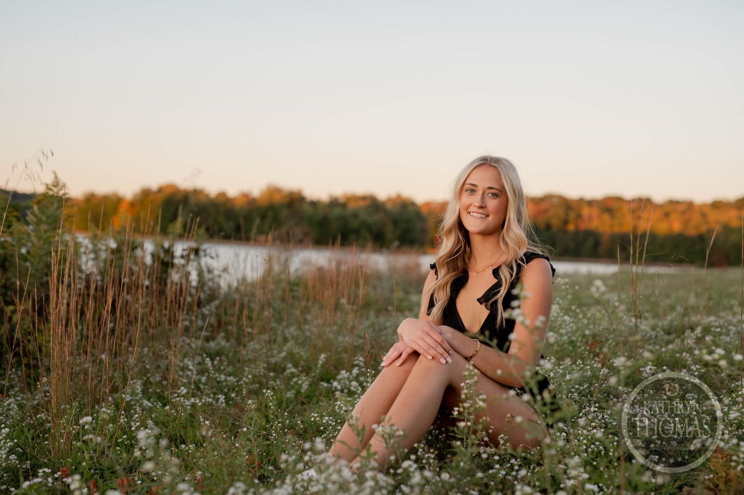 Outdoor portrait session in golden wildflower field at sunset with lake backdrop.