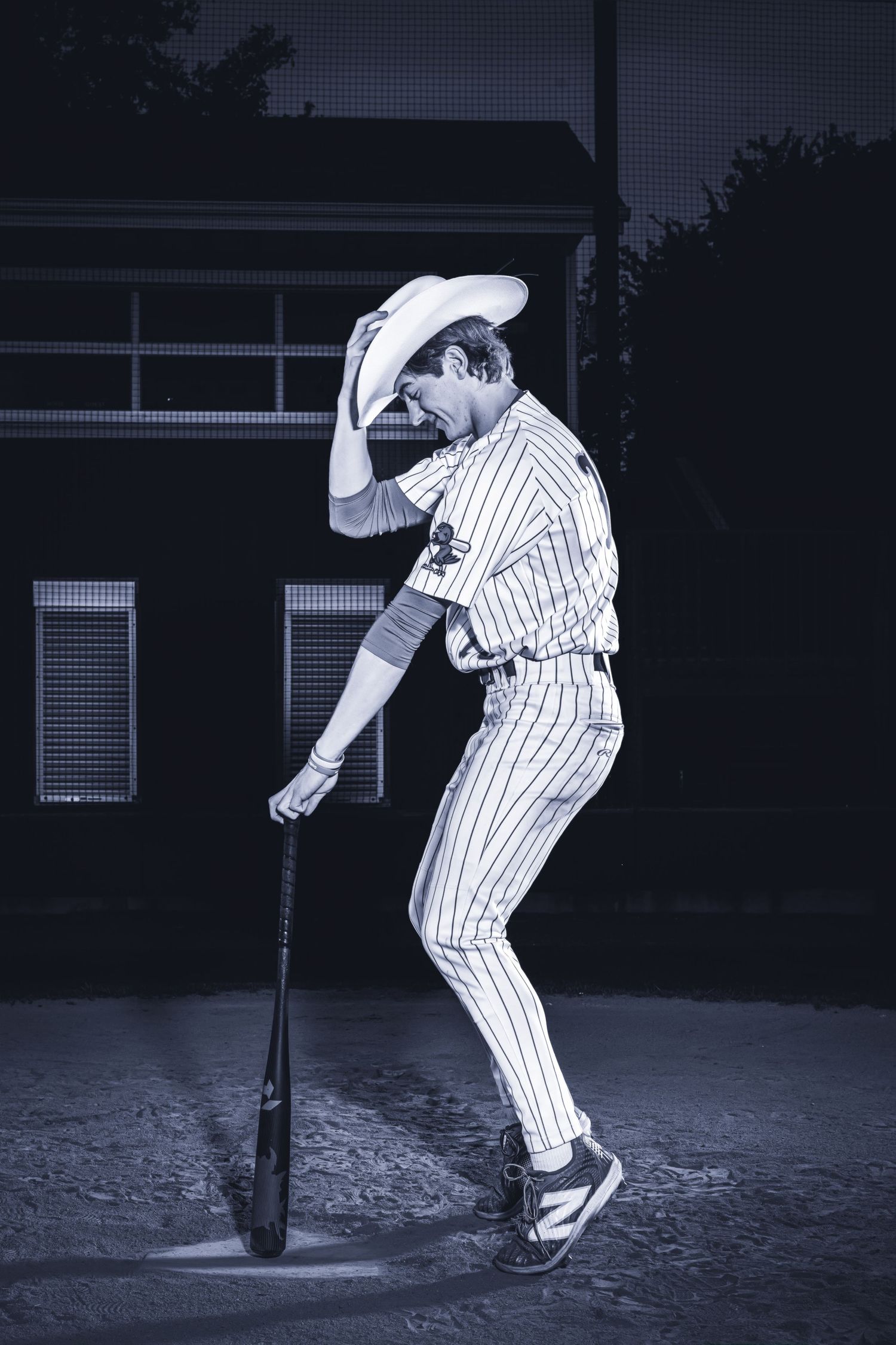 A baseball player in pinstripes takes a batting stance at sunset in a dramatic black and white photo.