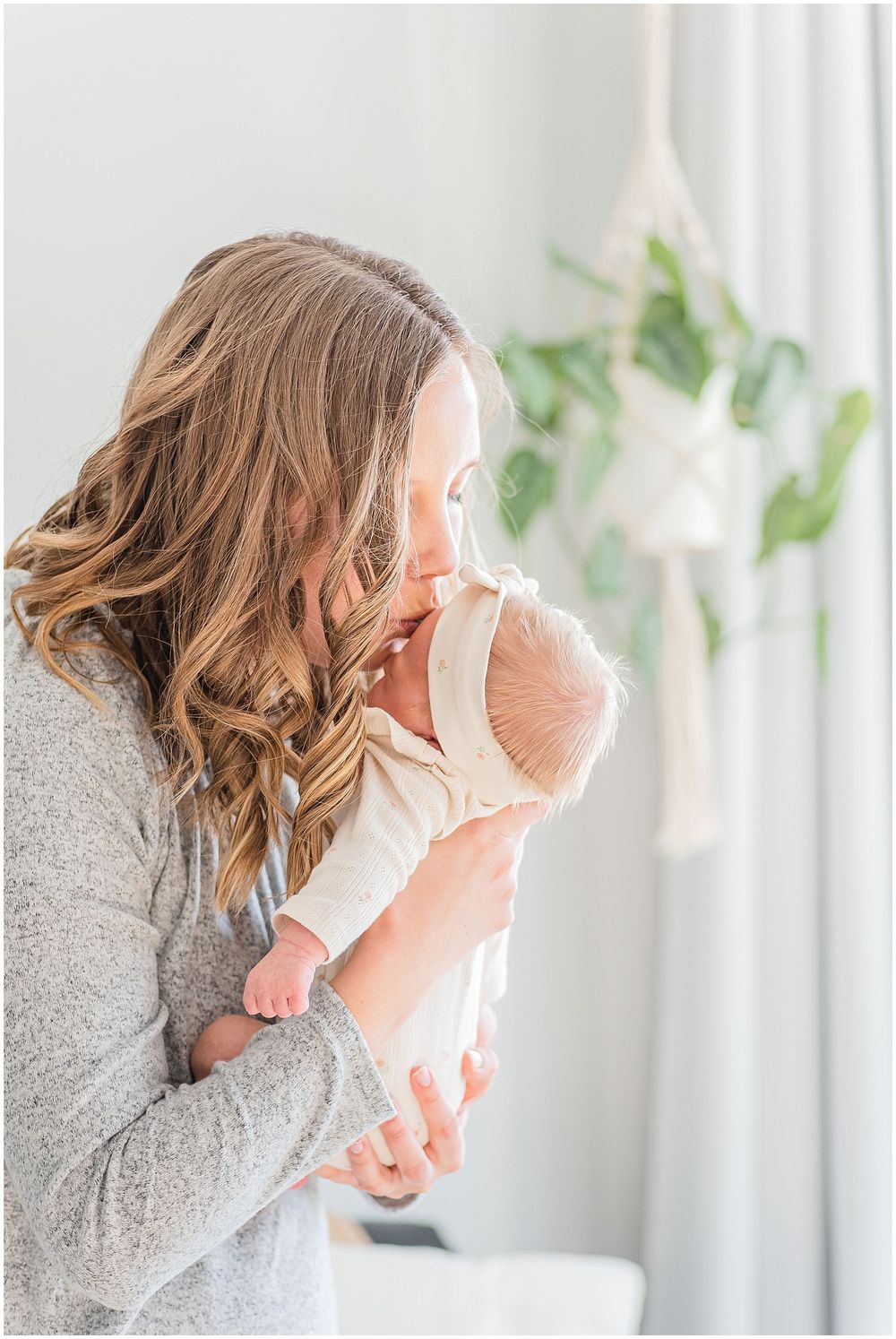 A tender moment between parent and baby near a window with hanging plants.