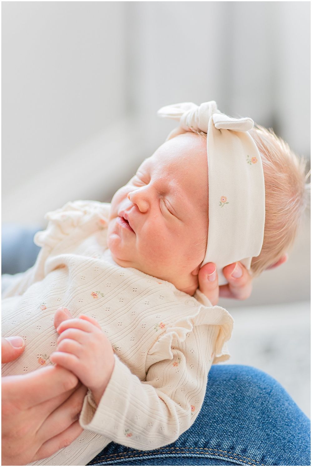 A sleeping baby wearing a cream-colored bow headband and knit outfit.