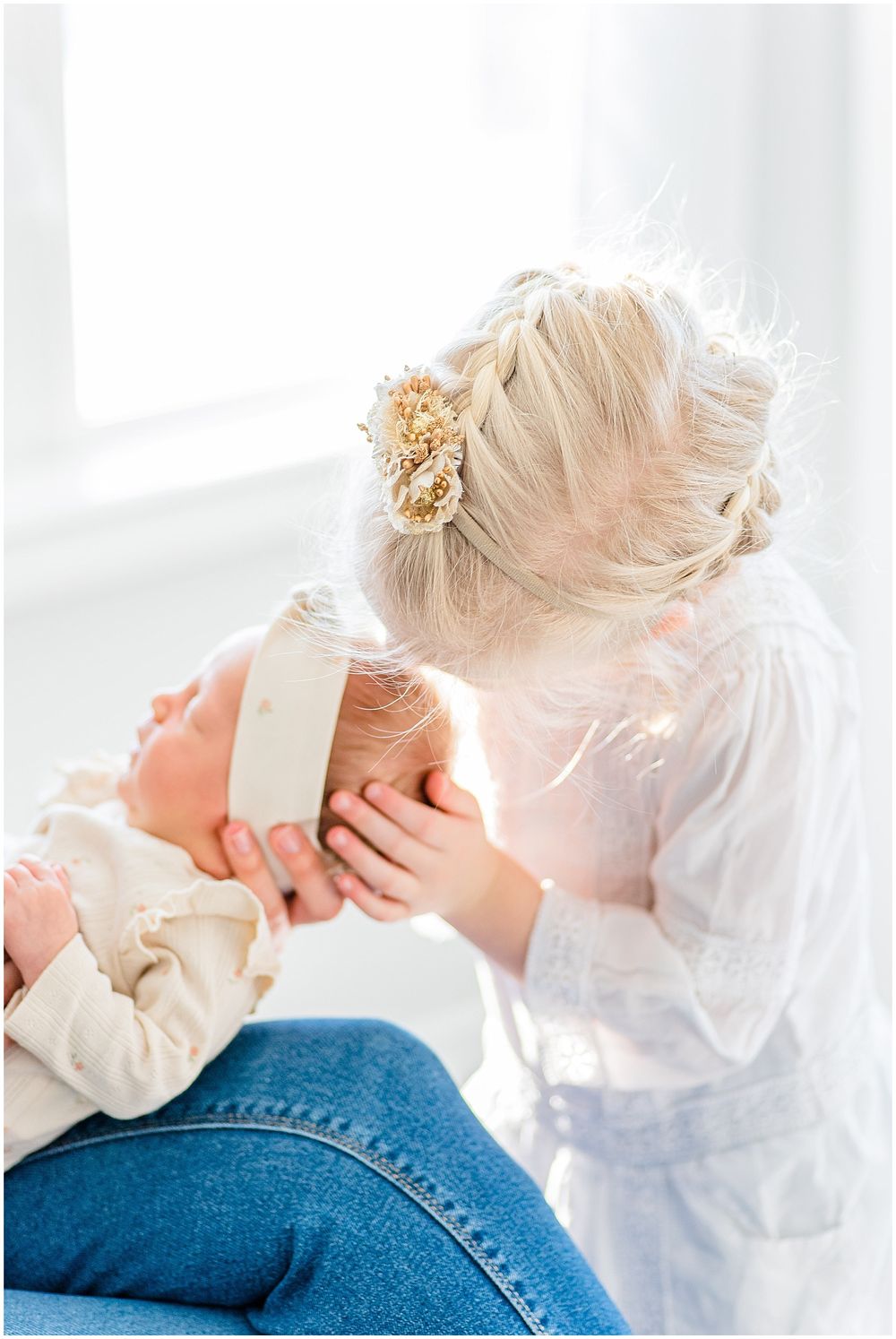 A tender moment between sister and baby captured in soft natural window light.