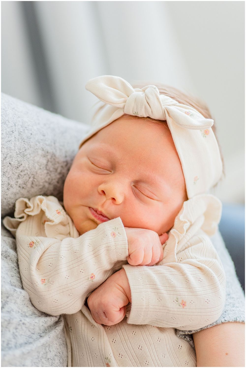 Peaceful sleeping newborn wearing a cream bow headband and ruffled outfit.