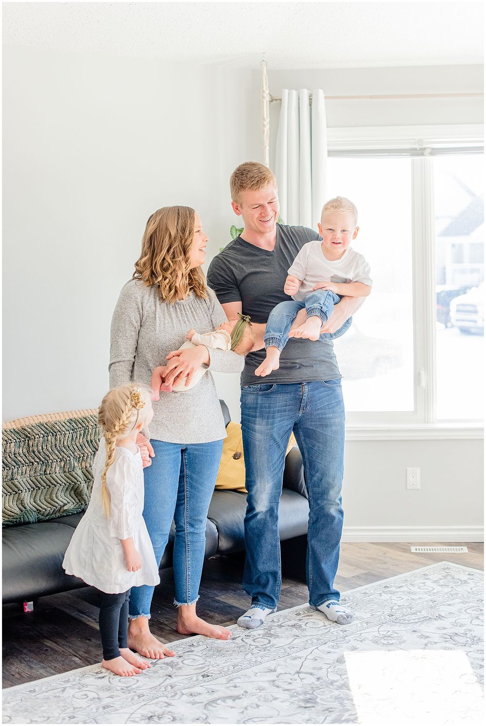 Family portrait in bright living room with parents and children gathered together on gray carpet.