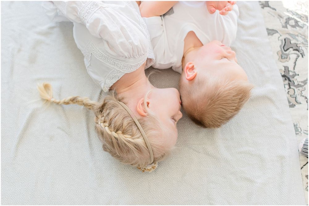 Two babies in white outfits lying together on light colored blanket.