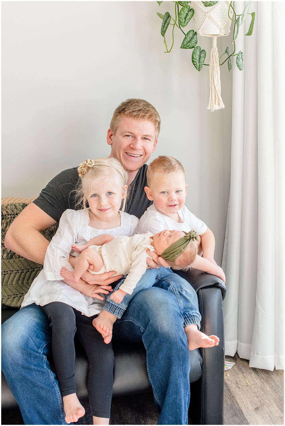 Tender family moment captured on gray couch with decorative plant hanging in background.