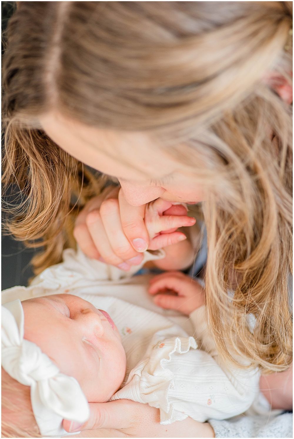 Intimate close-up of tender moment with sleeping newborn in white outfit.