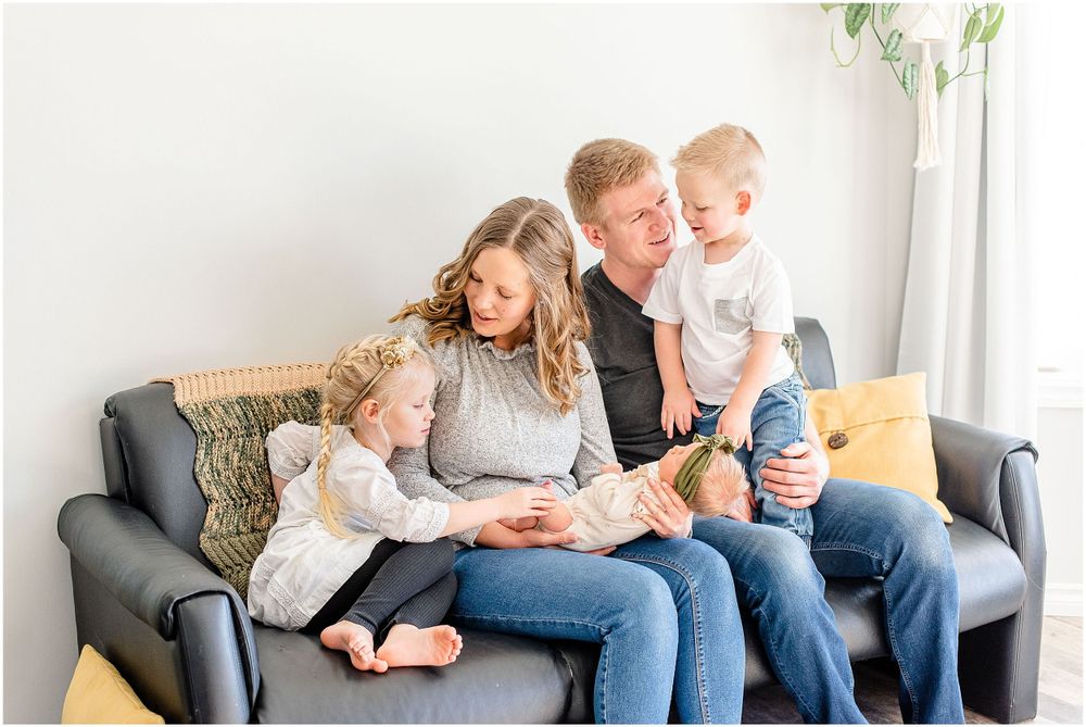 Family relaxes together on grey couch with yellow pillow in bright living room.