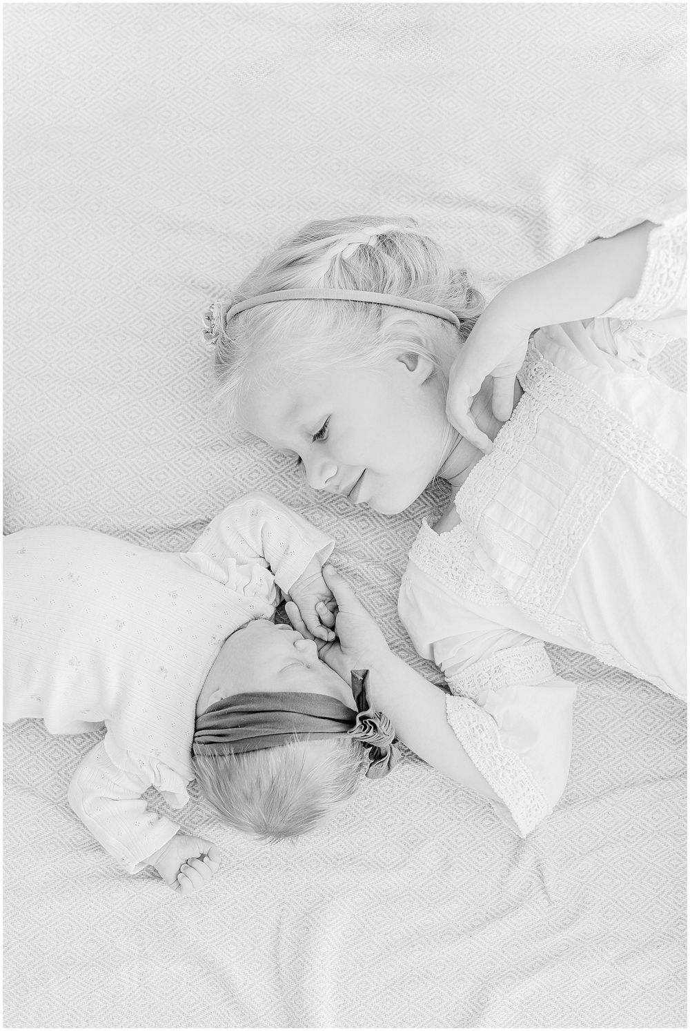 A black and white image of two siblings sharing a sweet moment while resting.