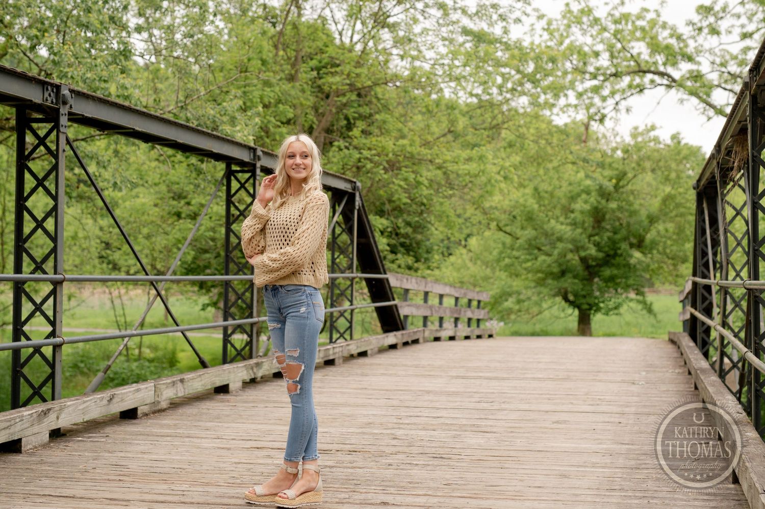 Spring fashion photo on rustic bridge wearing light knit sweater and distressed denim.