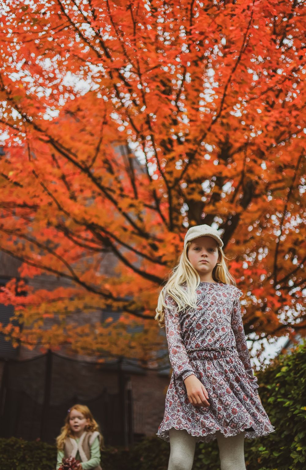 A person in a floral dress poses under vibrant red autumn foliage.