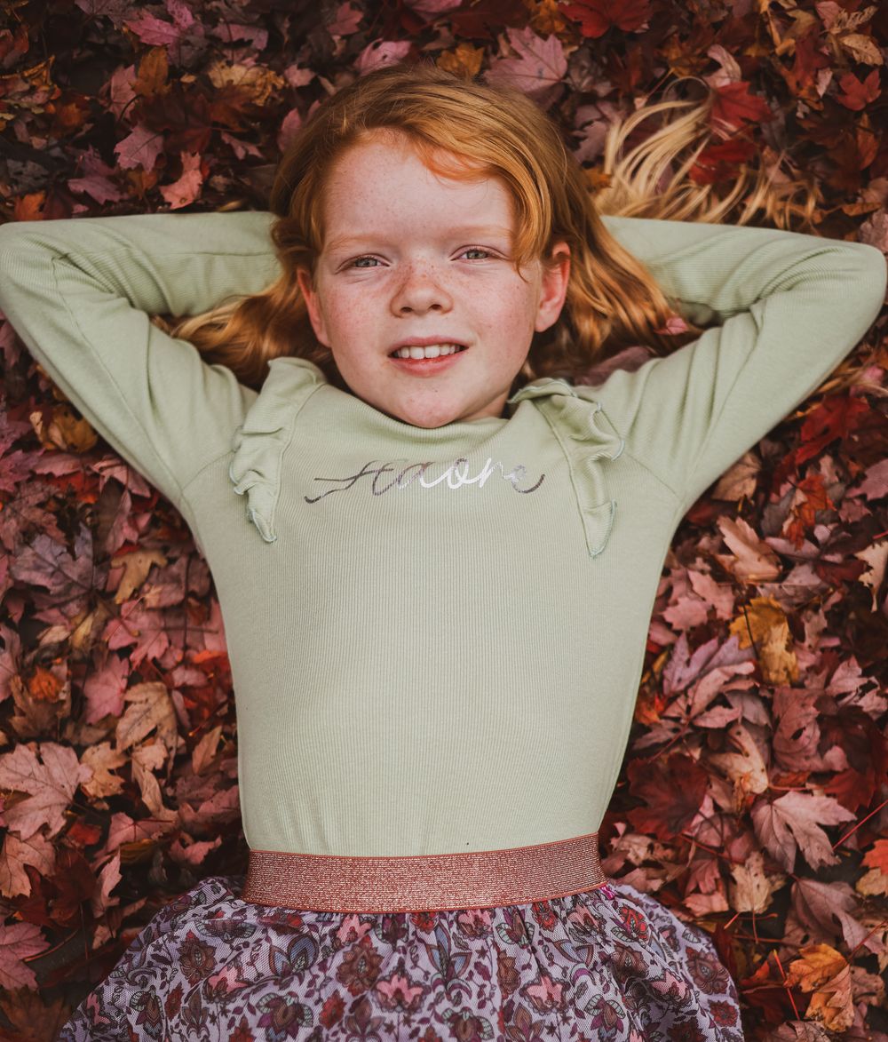 Carefree child lying on autumn leaves wearing mint green sweater and floral skirt.
