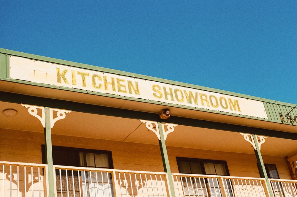 Vintage-style storefront with 'Kitchen Showroom' signage and decorative trim against a bright blue sky.