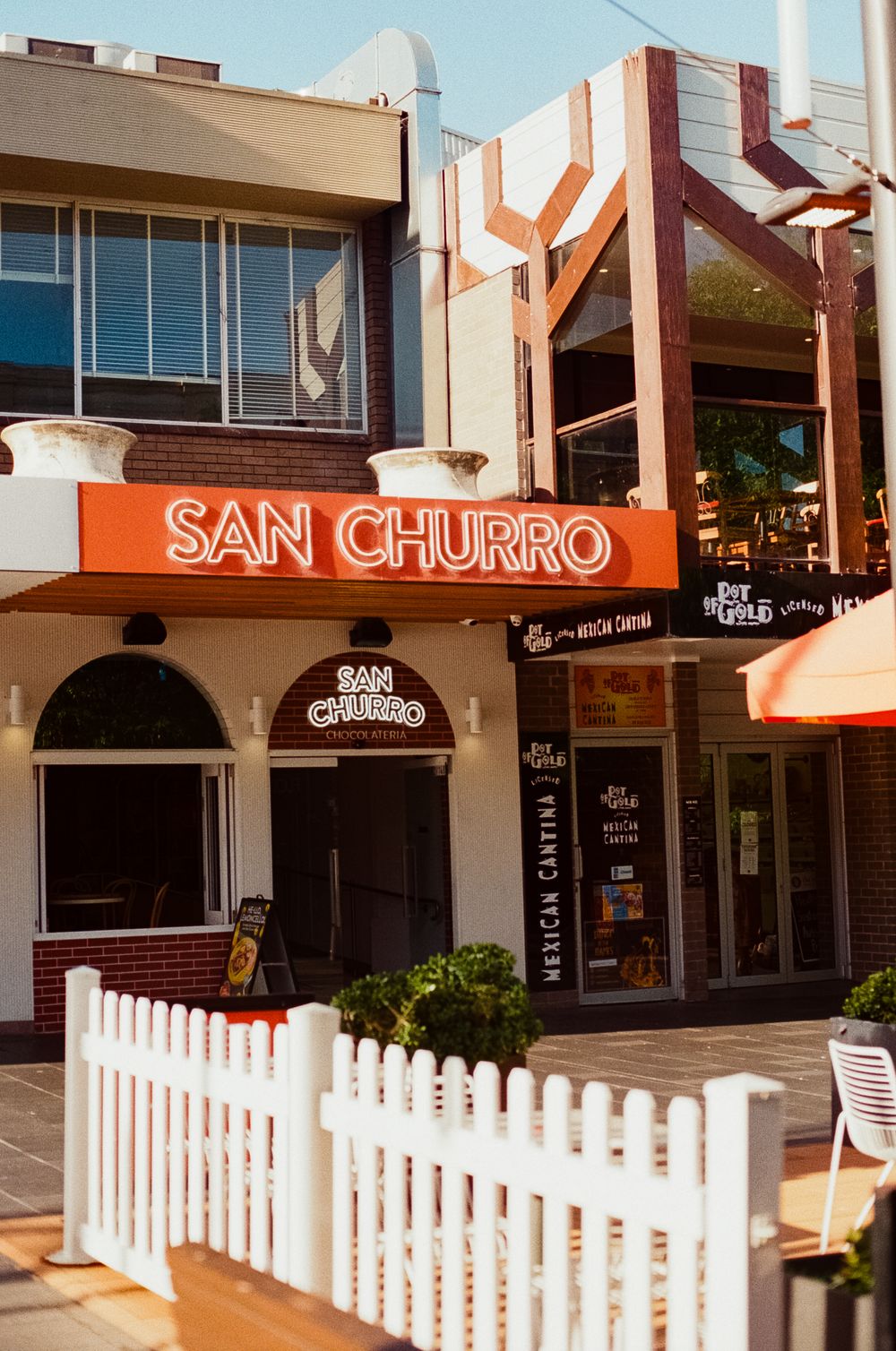 Storefront of San Churro cafe with white picket fence and outdoor seating area.