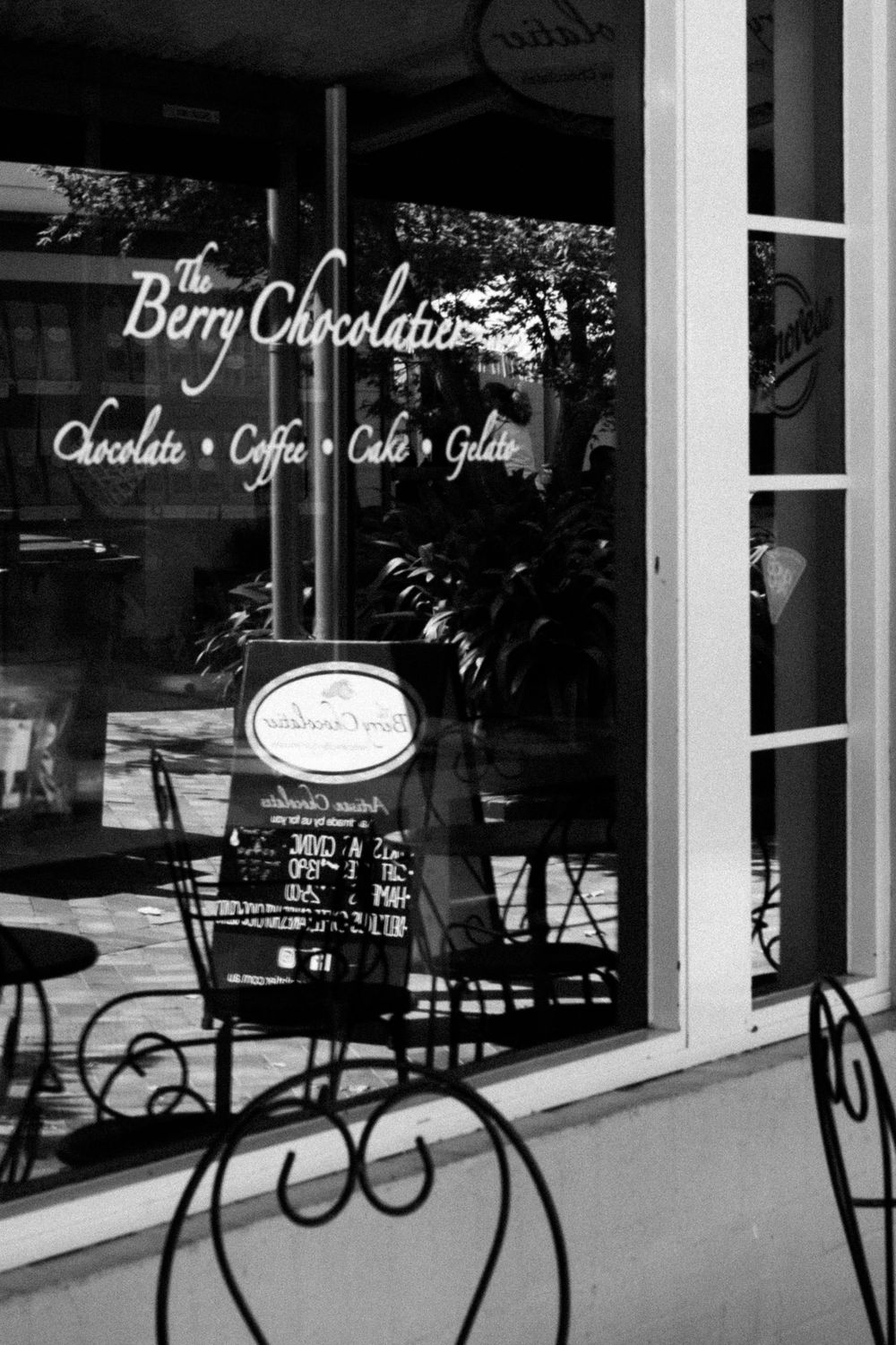 Black and white storefront of The Berry Chocolatier cafe with ornate metal chairs.
