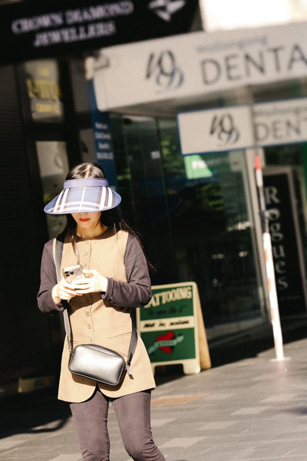 Person wearing grey outfit and sun visor checking phone outside dental office.