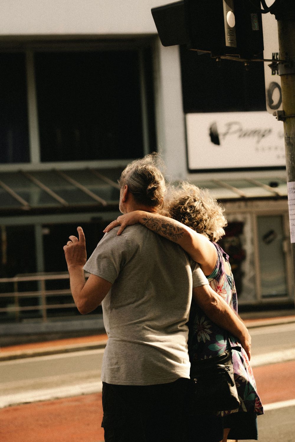 Two figures walk together on a sunny urban street.
