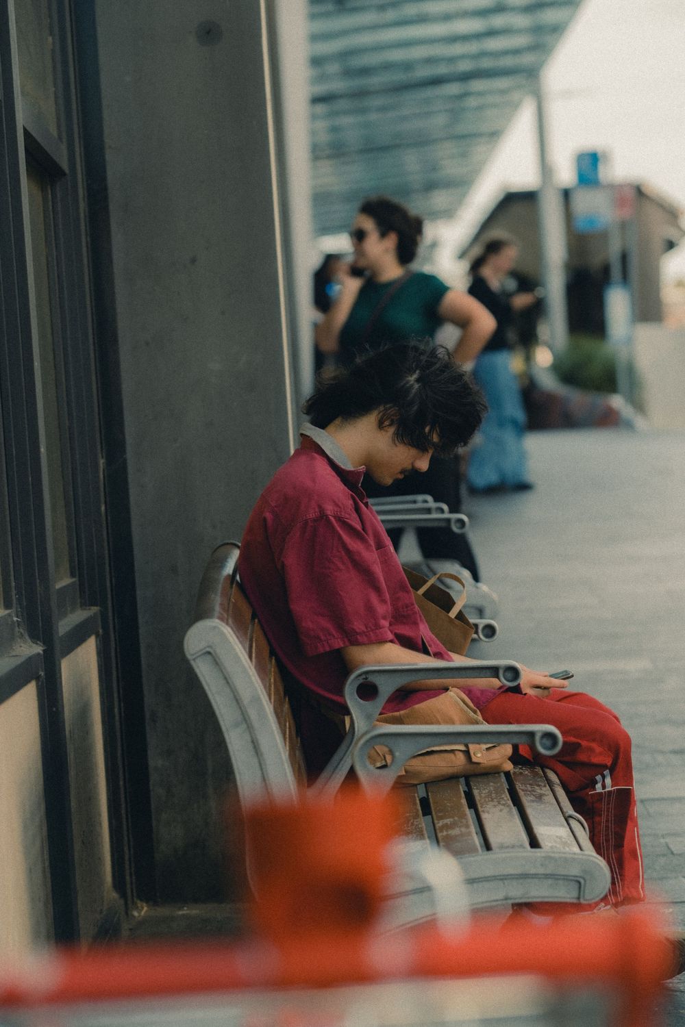 People sitting on outdoor benches along urban sidewalk on sunny day.
