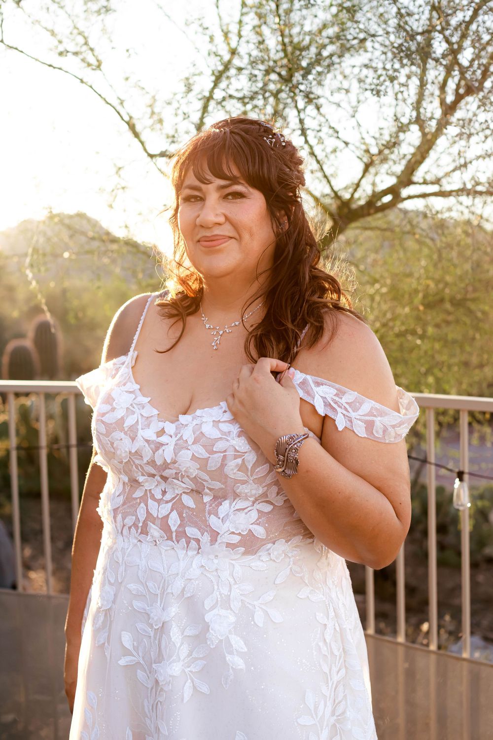 Bride in lace wedding dress poses at sunset on an outdoor balcony.