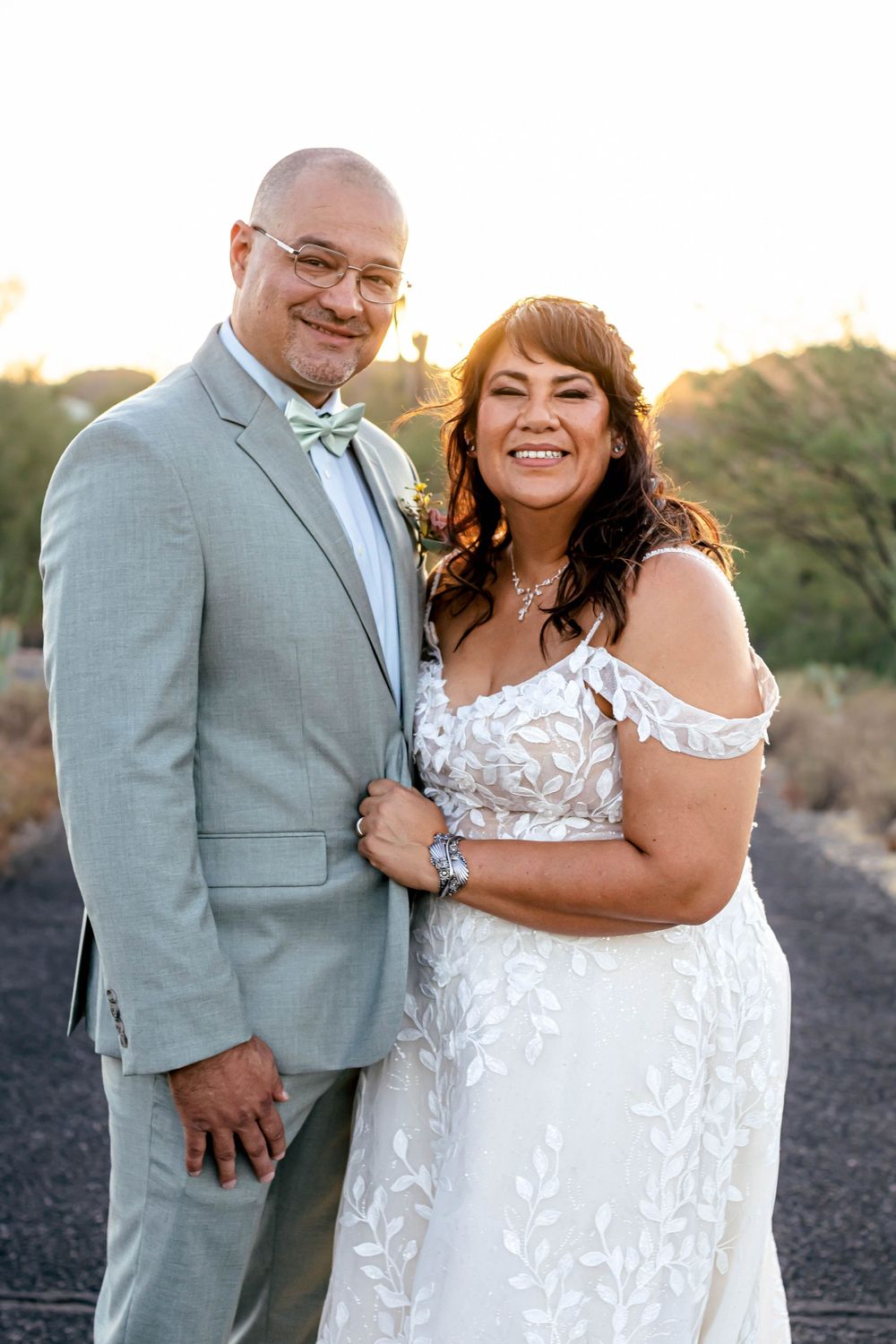 Newlyweds in formal attire smile together during golden hour.