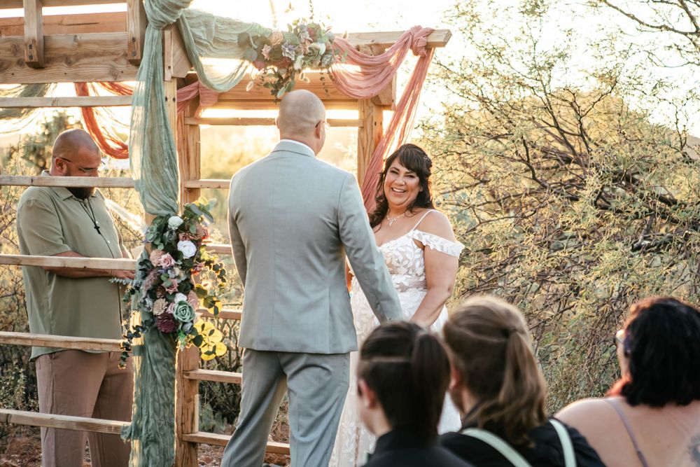 Outdoor wedding ceremony under a decorated pergola during golden hour.