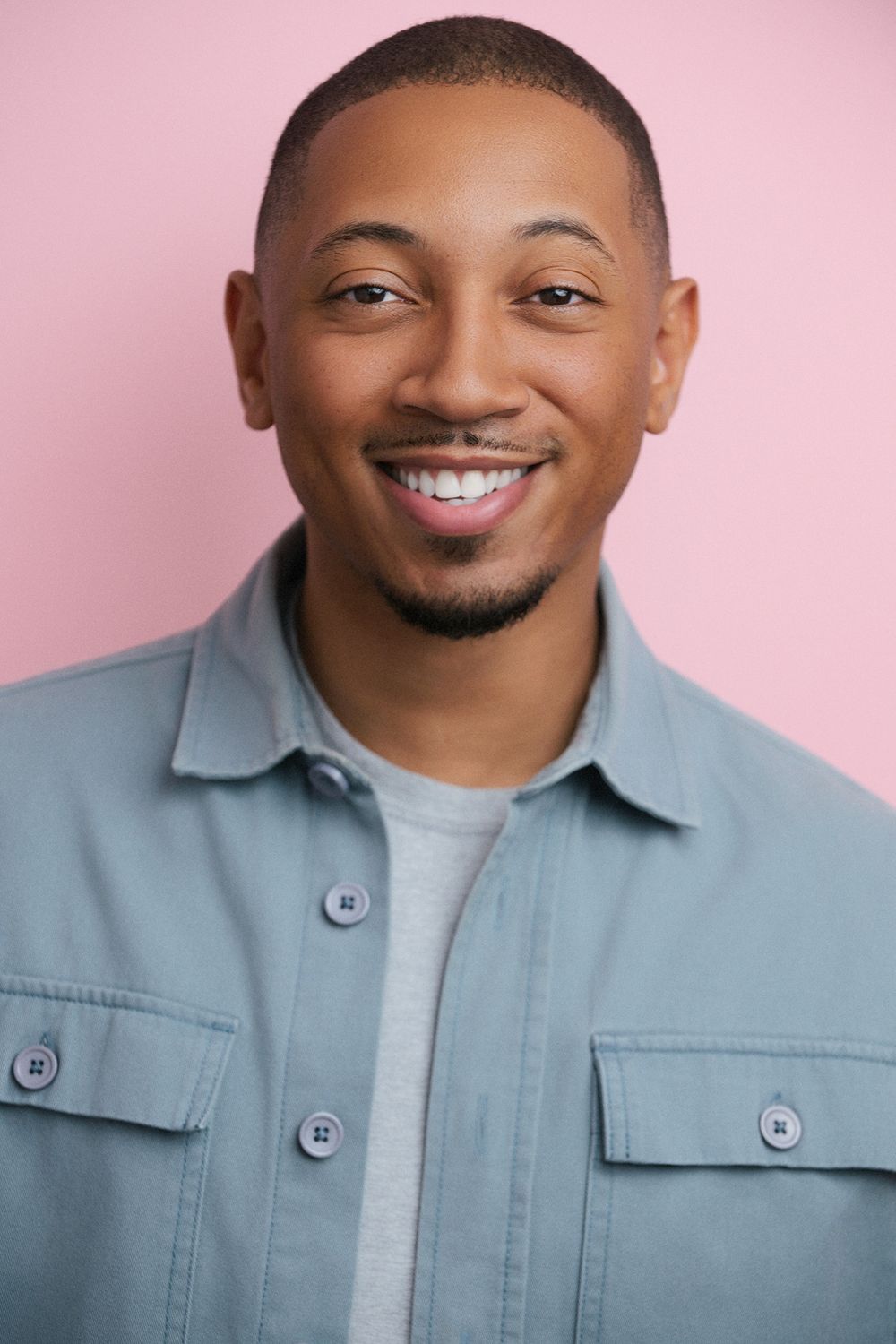 Casting-ready headshot of a Black male actor taken in studio, showcasing natural expression and clean colored pink background.