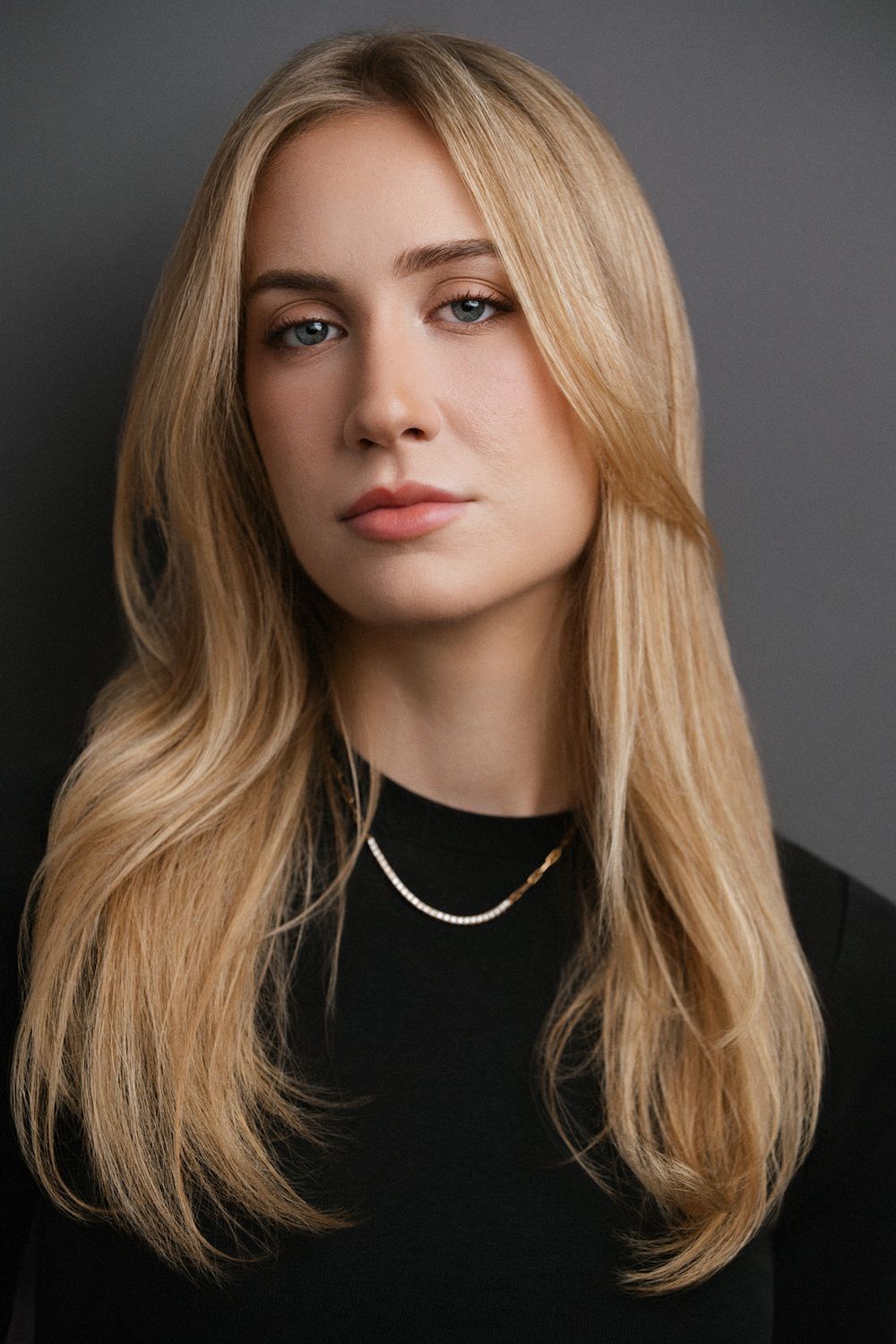 Cinematic actor headshot photographed in studio with subtle lighting and a textured gray backdrop.