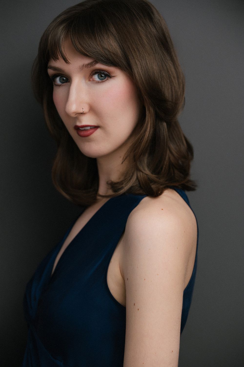 Professional headshot of a White female actor photographed in studio for commercial and theatrical styled brown hair and burgundy lipstick.