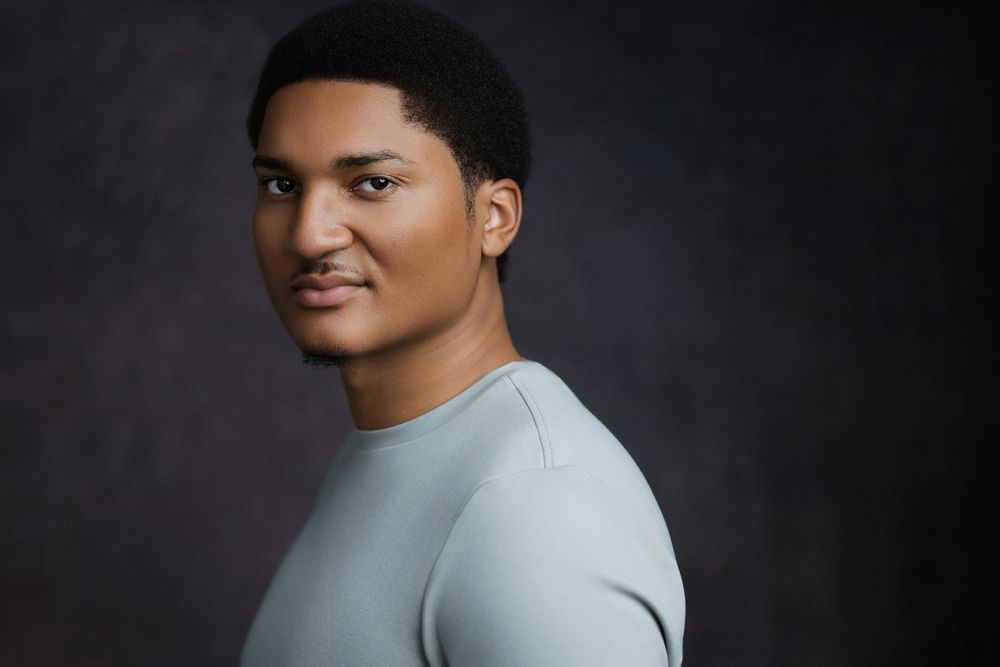 Professional studio actor headshot of a Black male actor photographed against a textured color backdrop with cinematic lighting.