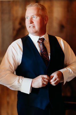 A person wearing a navy vest and white dress shirt adjusts their formal attire.