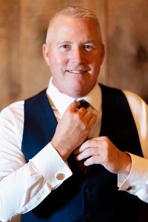Groom in formal attire adjusting tie and cufflinks before wedding ceremony.