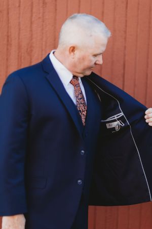 Person in navy suit showing the interior lining of their jacket against a red wall background.