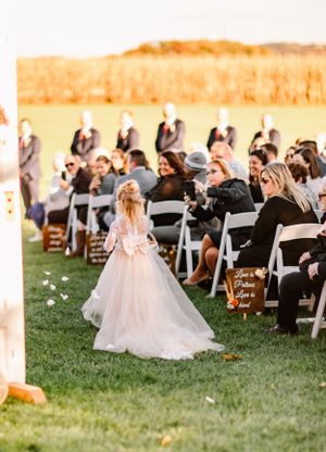 Wedding ceremony setup outdoors with white chairs and flower petals lining the aisle.