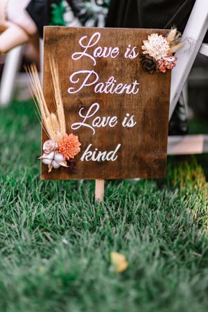 Rustic wooden wedding sign with 'Love is Patient Love is Kind' text decorated with dried flowers.