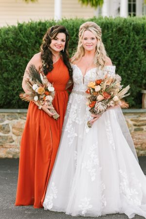 Two women pose together at wedding, one in orange dress and one in white bridal gown.