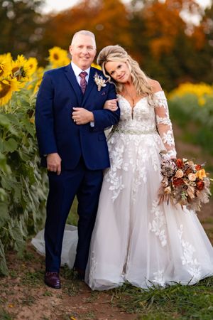 Wedding couple poses in sunflower field during autumn, with bride wearing lace gown.