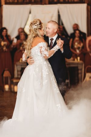 Couple dances in elegant barn venue with fog effects and warm lighting.