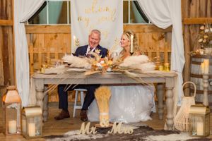 A couple sits at their rustic wedding sweetheart table decorated with candles and fall decor.
