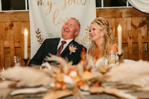 A couple shares a joyful moment at their rustic reception table decorated with autumn elements.