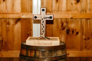 A decorative wooden cross sits atop a rustic barrel at a wedding ceremony venue.