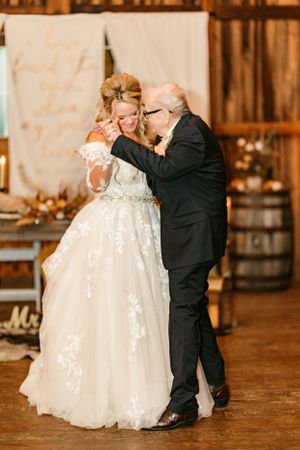 A couple shares their first dance in a rustic barn venue with warm lighting.