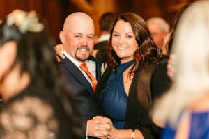 A couple shares a romantic moment on the dance floor at a formal event wearing navy blue and orange attire.